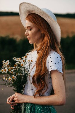 Bir köy yolunda yürürken elinde papatya buketi tutan bir kızın portresi. Güzel yaz manzarası. Yaz gezisi.