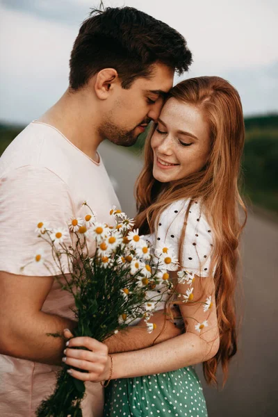 Casal de amantes no meio de uma estrada rural segurando uns aos outros à mão. Retrato de uma menina com um buquê de margaridas. Uma bela mulher. Lindo. — Fotografia de Stock