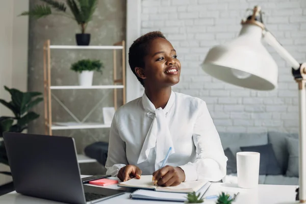 Mujer sonriente de oficina negra sentada en el portátil tomando notas en el trabajo. Tecnología de Internet. Chica afroamericana. — Foto de Stock