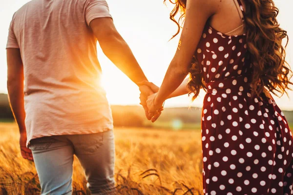 Baksidan av ett par förälskade promenader på ängen. Man och kvinna i kärlek håller varandra i handen. — Stockfoto