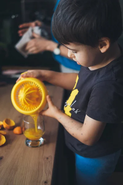 Rapazinho caucasiano a deitar sumo de laranja fresco num copo. Comida saudável. Dieta saudável. Sumo de fruta. — Fotografia de Stock