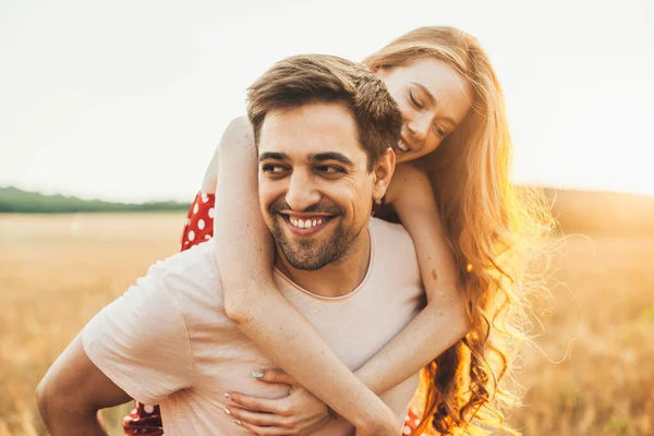 En man som håller en kvinna på ryggen på sommaren på ett vetefält. Älskade par. Svin tillbaka rider. — Stockfoto