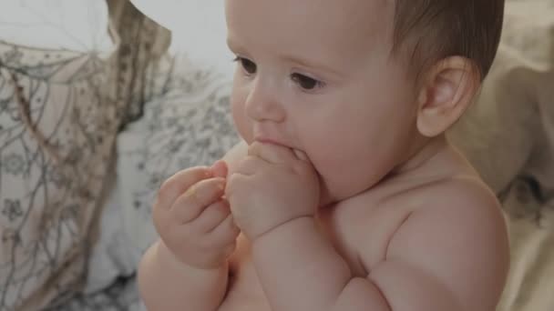 Baby sitting dans un lit confortable avec seulement une couche et tenant un morceau de banane dans sa main. Alimentation saine, alimentation. Aliments sucrés. — Video