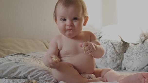 Bambino seduto sul letto che si diverte mentre mangia banane che si sporcano sulla bocca. Un bambino sorridente e felice. Alimenti dolci. — Video Stock