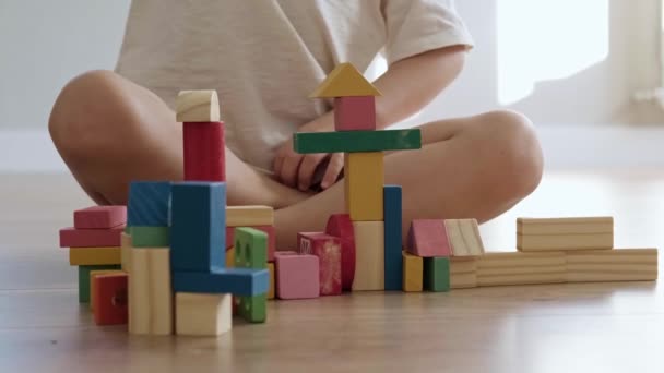 Rapaz irritado destrói o que ele construiu a partir de estatuetas coloridas em pé no chão na sala de jogos. Desenvolvimento infantil. — Vídeo de Stock