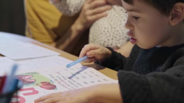 Çocuk alıştırmanın durumunu okuyor ve bir kalemle yazmaya başlıyor. Aile hobisi. — Stok video