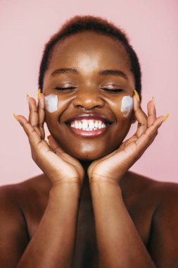 Yüzüne nemlendirici krem sürerek gülen kadın pembe arka planda izole edilmiş. Güzellik tedavisi. Güzel surat..