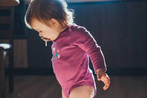 Vista lateral de uma menina de pé na cozinha em casa à procura de algo no chão. Dia da família. Estilo de vida saudável. Cuidados com o bebê. — Fotografia de Stock