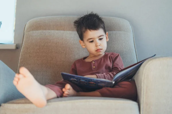 Vista frontal de un niño leyendo un libro mientras se relaja en el sofá en casa. Desarrollo infantil. Aprender divertido. —  Fotos de Stock