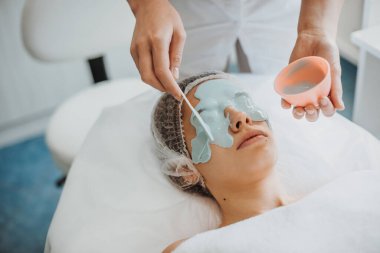 Güzellik uzmanlarının ellerinin portresi yetişkin bir kadının yüzüne aljinat maske takıyor. Spa vücut bakımı. Doğal güzellik. Yenilenme tedavisi. Yüz Yüzü