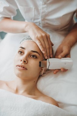 Kadın yüzü, profesyonel bir kozmetikçinin ellerinden ultrasonik yüz temizleme ameliyatı oluyor. Yüz derisi. Güzel surat. Dermatoloji, kozmetoloji