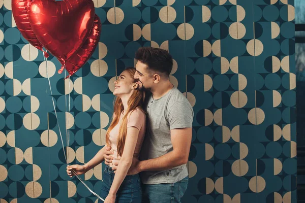 手にハート型のヘリウム風船を持ちながら 後ろから抱きかかえた青い壁 赤い髪の少女をポーズをとるカップル 美顔だ 家族の日 — ストック写真