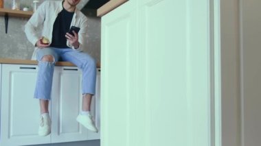 Mutfakta oturan ve elinde kırmızı elmayla müşterilerle konuşan bir adamın görüntüsü. Ev kavramı. Cep telefonu çağrısı.
