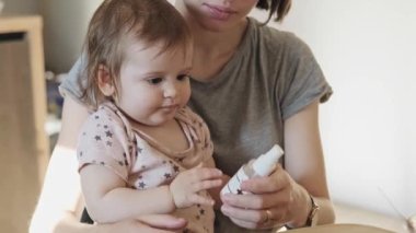 Anne masadan plastik dezenfektan şişesini alıyor ve enfeksiyonu önlemek için evde tuttuğu bebeğin ellerine uyguluyor.