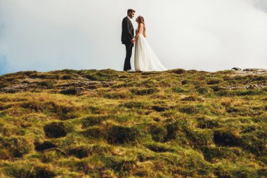 Yeni evli çiftin dağ tepesinde durup eğlenirken yan görüntüsü. Uzak görüş. Düğün günü..