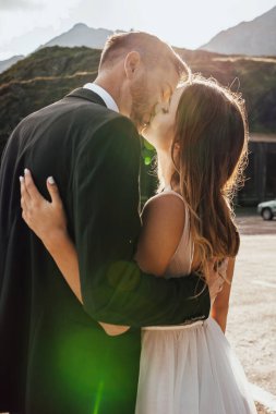 Güzel bir gelin ve damadın dağ yolculuklarına giderken bir öpücük için durduğu arka manzara. Kırsal alan. Dağ manzarası. Dağ yolu.