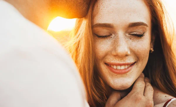 Retrato de cerca de una chica pecosa feliz siendo besada en la frente por su marido. Concepto de viaje. Cierre el retrato. Campo de trigo. — Foto de Stock