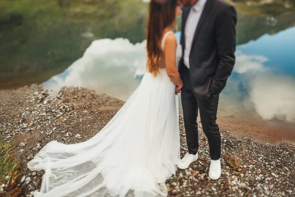 Retrato dos recém-casados, a noiva eo noivo posando perto uns dos outros perto de um belo lago nas montanhas. Romântico casamento sessão de fotos na natureza. — Fotografia de Stock