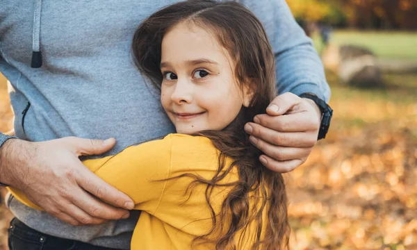 Πορτρέτο ενός κοριτσιού που αγκαλιάζει τον πατέρα της και κοιτάζει την κάμερα χαρούμενα. Κόρη αγκαλιάζει τον μπαμπά στο πάρκο για το σχεδιασμό του τρόπου ζωής. Χαρούμενη αγαπημένη οικογένεια. — Φωτογραφία Αρχείου