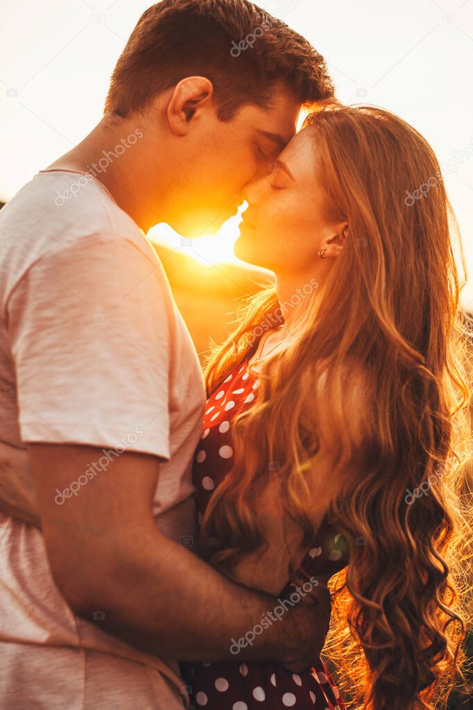 Side view of a couple of newlyweds standing and hugging before a kiss against the background of the sunset in the wheat field. Portrait for lifestyle design.