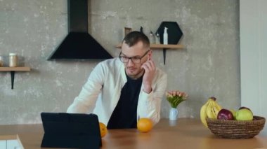 Adam İngiltere 'den arkadaşlarını selamlıyor, onunla mutfakta oturup kablosuz kulaklıkla konuşan bir video görüşmesi yapıyor. Çevrimiçi