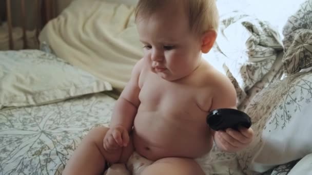 婴儿光着身子坐在床上，只穿着尿布玩耍着用脚按压毛绒玩具。美肤护理。照看孩子。漂亮的脸蛋家庭日。开心的脸. — 图库视频影像