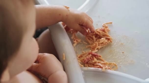 Vista dall'alto di un tavolo per bambini sporco e pieno di pasta con sous da cui il bambino prende con la mano e mangia con appetito. Sviluppo del bambino. Vista dall'alto. — Video Stock