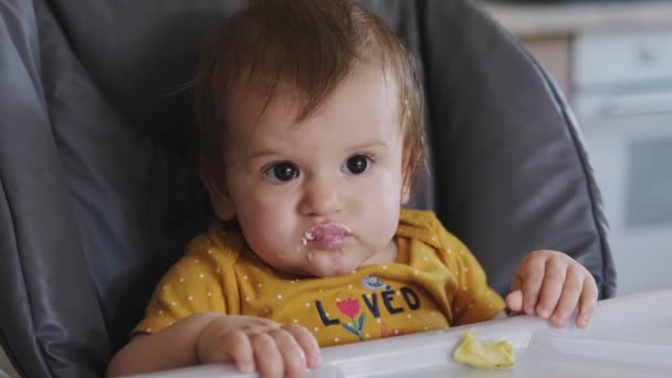 Baby flicka sitter i barnstol tugga sista munnen av måltid tittar runt nyfiket, mödrar hand lyfta leksak och sätta framför barnet. Hälsosam mat — Stockvideo