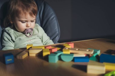 Masada bir sürü tahta figürlü bebek yüksek sandalyede oturup aşağıya bakıyor. Renkli bebek blok binası.