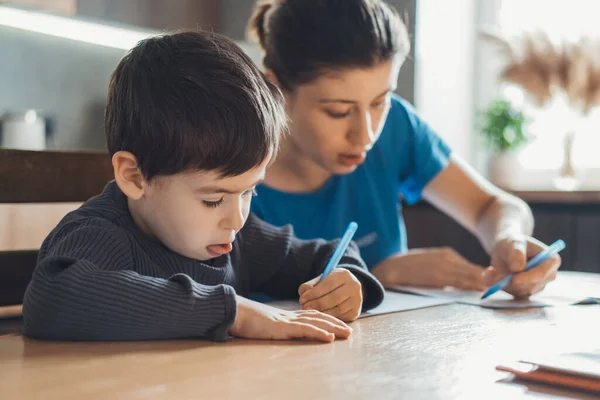 La madre pasó la tarde sentada en la cocina con su hijo y revisando los deberes. Mamá ayuda niño aprendizaje, gran diseño para cualquier propósito. —  Fotos de Stock