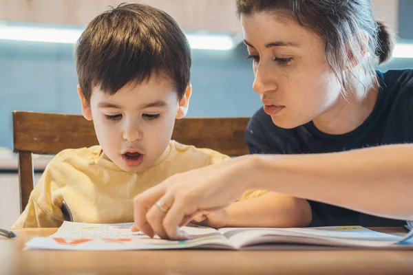 Madre ayudando con la tarea de su hijo señalando algo escrito en su cuaderno. Mamá ayuda niño aprendizaje. —  Fotos de Stock