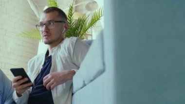 Kafkasyalı bir adam elinde telefonuyla yerde oturmuş arkadaşlarıyla konuşuyor. Mobil iletişim. Cep telefonu çağrısı.