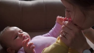 Evde yatağında kızının ayaklarını öpen gülümseyen bir annenin portresi. Aile bakımı. Cilt bakımı. Aile koruması. Bebek bakımı.