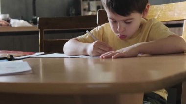 Masada oturup, evde ders çalışıp, ödevlerini yapan bir çocuk. Eğitim konsepti yazmak. İş yeri konsepti. Okul sınıfı..