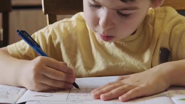 Nahaufnahme Porträt eines konzentrierten Jungen mit Bleistift, der zu Hause neue Buchstaben oder Wörter übt. Coronavirus-Konzept. Schulklasse. — Stockvideo