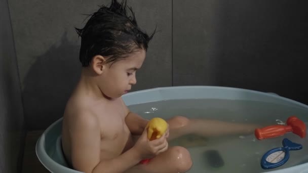 Кавказький хлопчик купається у воді, граючись з іграшками качки у ванні. Діти грають. Здорове волосся. Здоровий спосіб життя. Охорона волосся. — стокове відео