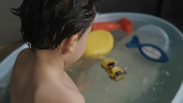 Rückansicht eines Jungen, der in der Badewanne sitzt und Spielzeugautos spielt. Haarpflege. Kinder spielen. — Stockvideo
