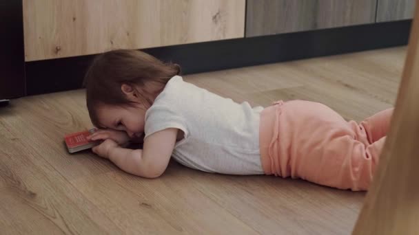 Portret van een klein meisje met een boek in haar handen, liggend op de vloer in een knus interieur. Droevig gezicht. Mooi jong meisje. Babyverzorging. Gezinszorg. — Stockvideo