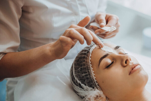 Beauticians hands applying facial cream mask over patients forehead at the spa salon. Medical treatment. Facial treatment. Beauty treatment. Facial skincare.