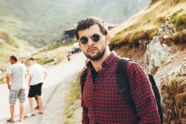 Bir adamın portresi dağlık yolda duran bir grup arkadaşla dağlarda seyahat eden bir kameraya bakıyor. Yaz tatili. Dağ yolu.