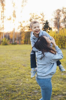 Oyuncu küçük çocuk annesiyle parkta vakit geçirmekten zevk alıyor. Anne, oğlunu sol omzunda taşıyor. Mutlu insanlar. Etkinlik ilişkisi.