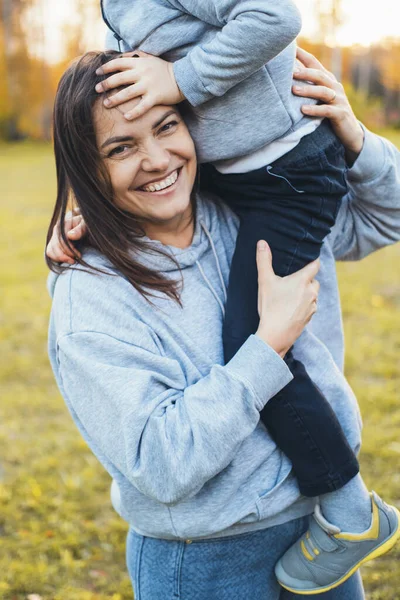 Πορτραίτο μητέρας που ποζάρει και χαμογελά στην κάμερα ενώ κουβαλάει το γιο της στον ώμο της. Κρατώντας τα χέρια. Σχέση δραστηριότητας. — Φωτογραφία Αρχείου