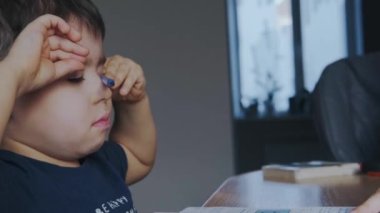 Karantina zamanında ödev yapmaktan yorgun düşmüş beyaz bir çocuk. Defterine yazı yazmış. Karantina, salgın hastalık. Karantina yaşam tarzı. Eğitim, öğrenim, öğrenim.