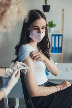 Tıbbi maske takmış profesyonel bir hemşire portresi ve aşağı bakan bir kadına grip aşısı yapan eldivenler. Virüs koruması. Doktor Corona 'yı veriyor