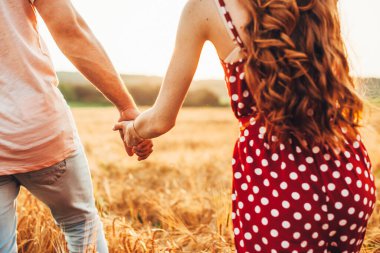 Buğday tarlasında yürürken el ele tutuşan çiftlerin yakın çekimi. Erkek arkadaşı kız arkadaşını gizli bir yere götürüyor.