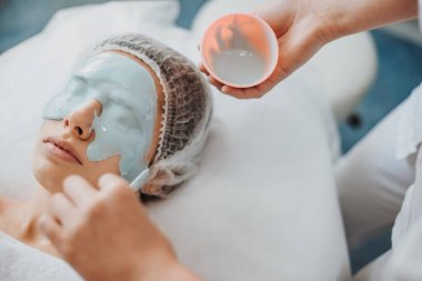 Yakın plan portre doktorlarının elleri bir kadının yüzüne aljinat maske takıyor. Dermatoloji, kozmetoloji. Kozmetik güzellik prosedürü. Yüz tedavisi.