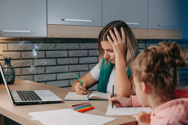 Madre usando el portátil para ayudar a su hija en la tarea sentada en la mesa en la cocina. Educación en el hogar. —  Fotos de Stock