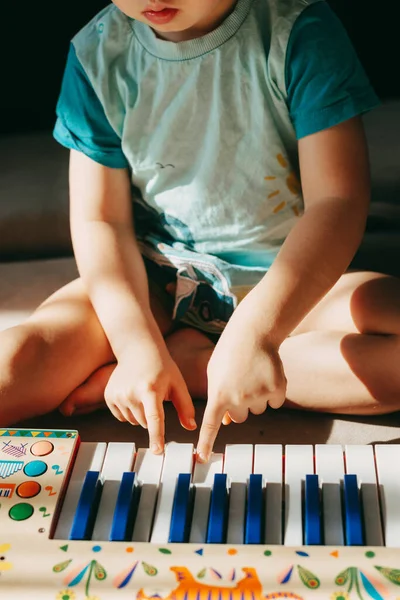 Vista de perto de um garotinho sentado no chão brincando no teclado. Conceito Hobby. Conceito de educação. Conceito de alegria. — Fotografia de Stock