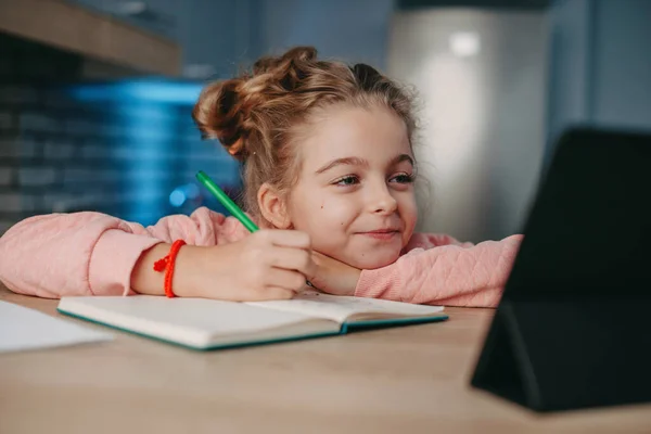 Χαμογελαστό κορίτσι κάθεται στο γραφείο κάνει την εργασία, ενώ κάνει online εκπαίδευσηχρησιμοποιώντας tablet. . Σχολή Coronavirus. Καραντίνα, πανδημία. Μακρινός χώρος εργασίας Έξυπνο σπίτι. — Φωτογραφία Αρχείου