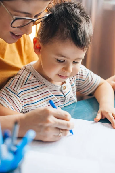 Retrato de cerca de una madre con anteojos que estudia y enseña a su hijo a escribir en casa. Educación infantil. Escuela del Coronavirus. Personas que trabajan. —  Fotos de Stock